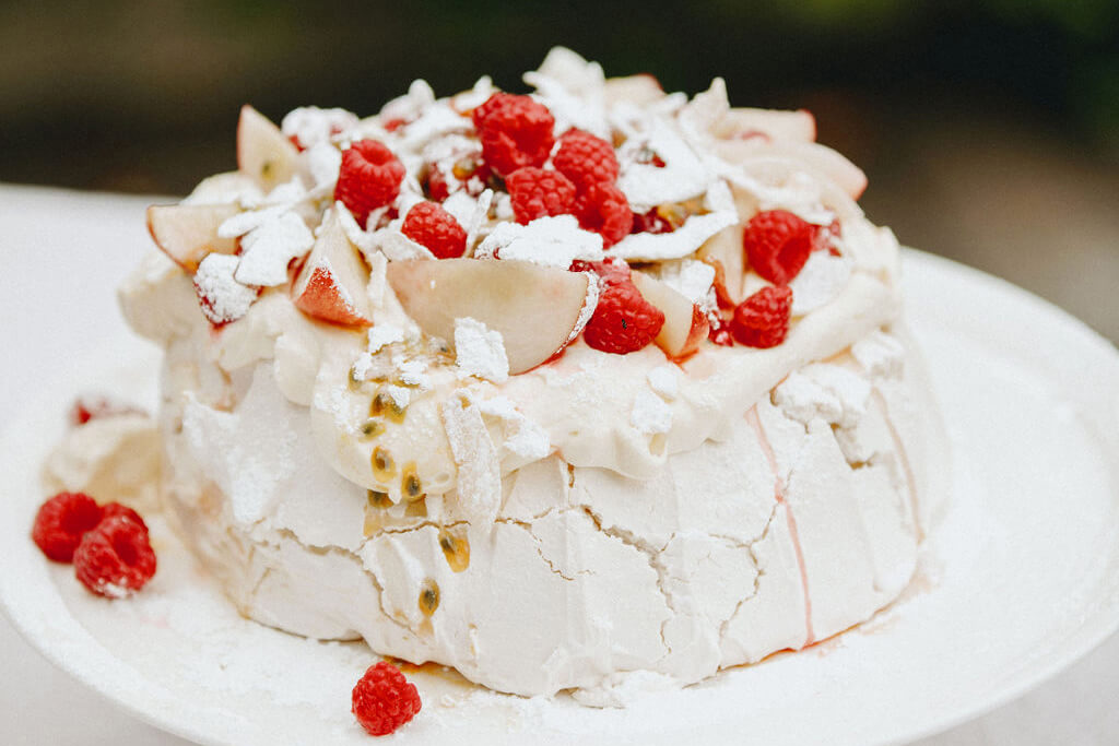 Blog Pavlova with peaches, raspberries, passion fruit, and sugar on a cracked meringue base.