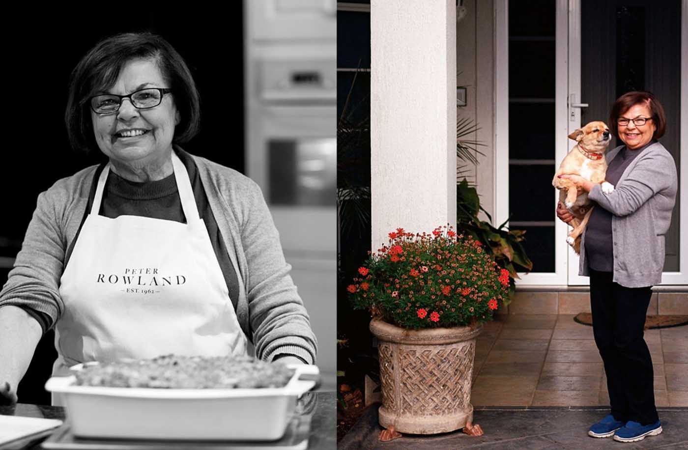 Blog Smiling woman in "Peter Rowland" apron cooks with a dog, near flowers by her front door.