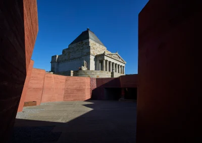 Grand stone monument under blue sky, framed by bold red architectural elements in front.