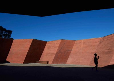Silhouette walks past bold red walls under a clear blue sky.