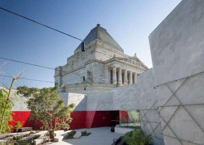 Shrine of Remembrance stands amid modern courtyard with greenery and red accents.