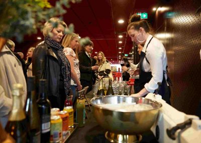 Bartender serves drinks at stylish bar as guests chat amid bottles and ice bowl.